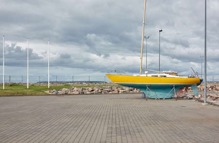 Yellow sailboat standing on land in a yacht marina. Kuivastu harbor, Estonia. Transportation, repair and service, cruise, recreation, amateur sailingの写真素材