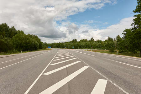 Empty highway through the forest on a sunny day. Asphalt road surface marking. Estonia, Europe. Transportation, traffic law, wanderlust, remote places, summer vacations conceptsの写真素材