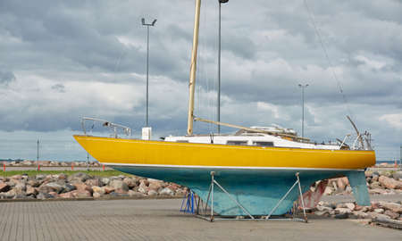 Yellow sailboat standing on land in a yacht marina. Kuivastu harbor, Estonia. Transportation, repair and service, cruise, recreation, amateur sailingの写真素材