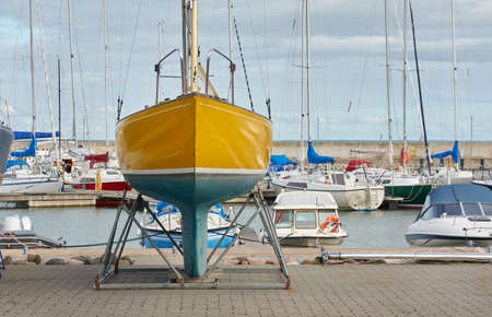 Yellow sailboat standing on land in a yacht marina. Kuivastu harbor, Estonia. Transportation, repair and service, cruise, recreation, amateur sailingの写真素材