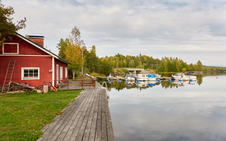 Wooden house colored with falu red dye. Motor boats, cutters and small fishing boats moored to a pier in a camping site. Forest in the background. Suiro lake (Kulovesi), Finland. Nature, ecotourismの写真素材