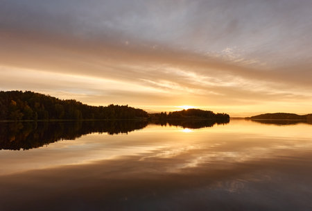 Majestic evergreen forest and lake at sunset. Soft golden sunlight, clear sky, glowing clouds.. Autumn. Suiro lake (Kulovesi), Finland. Panoramic view. Pure nature, ecotourism conceptsの写真素材