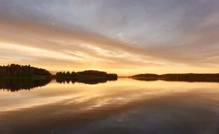 Majestic evergreen forest and lake at sunset. Soft golden sunlight, clear sky, glowing clouds.. Autumn. Suiro lake (Kulovesi), Finland. Panoramic view. Pure nature, ecotourism conceptsの写真素材