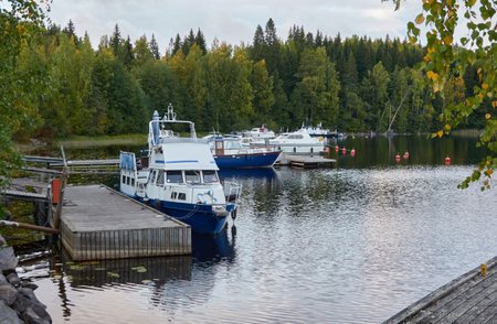 Boats, motorboats and cutters moored to a pier in river (canal). Forest park. Promenade and walking area. Early autumn landscape. Finland. Nature, leisure activities, eco tourism themesの写真素材