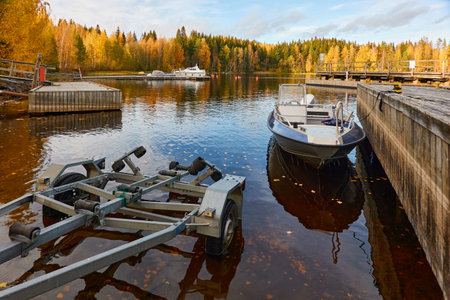 Motor boat or cutter moored to a pier in a camping site. Forest in the background. Fishing, swimming and boating area. Finland. Nature, vacations, recreation, ecotourism, lifestyle conceptsの写真素材
