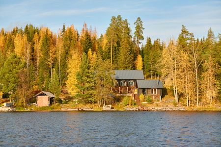 Rocky lake shore on a sunny day. Wooden house. Stones, forest, mighty pine and birch trees. Autumn landscape. Finland, Finnish nature. Ecology, fresh air, ecotourism, countryside life themesの写真素材