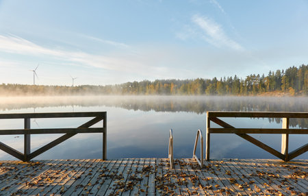 Forest lake in a morning fog. Wooden pier and swimming area. Wind farm, wind turbine generators. Finland. Scandinavia, Europe. Autumn landscape. Nature, ecology, ecotourism, alternative energy themesの写真素材
