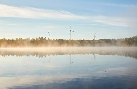 Forest lake in a morning fog. Wind farm, wind turbine generators. Clear blue sky, sunshine. Finland. Scandinavia, Europe. Autumn landscape. Nature, ecology, alternative and renewable energyの写真素材