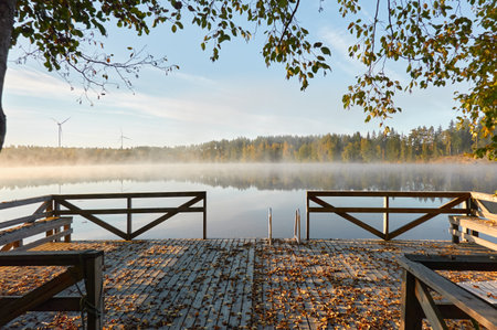 Forest lake in a morning fog. Wooden pier and swimming area. Wind farm, wind turbine generators. Finland. Scandinavia, Europe. Autumn landscape. Nature, ecology, ecotourism, alternative energy themesの写真素材
