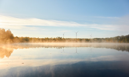 Forest lake in a morning fog. Wind farm, wind turbine generators. Clear blue sky, sunshine. Finland. Scandinavia, Europe. Autumn landscape. Nature, ecology, alternative and renewable energyの写真素材