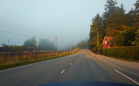 Empty asphalt road (highway) through the forest. Thick fog. Wooden country house and railroad. Concept autumn landscape. Transportation, logistics, remote places, freedom, travel, tourism themesの写真素材