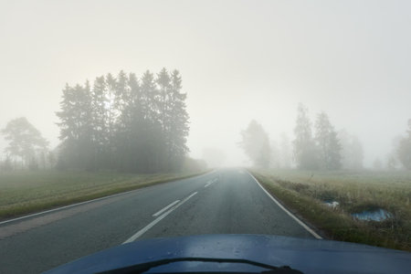 Empty asphalt road (highway) through the fields and forest. Thick fog. View from car. Autumn landscape. Transportation, dangerous driving, speed, freedom, travel, tourism, the way forward themesの写真素材
