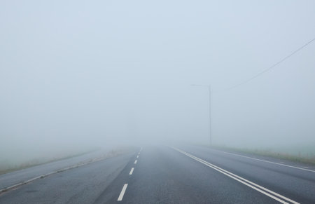 Empty asphalt road (highway) in a thick fog. Electricity power line close-up. Concept urban autumn landscape. Transportation, dangerous driving, speed, freedom, travel, tourism, the way forward themesの写真素材