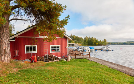 Wooden house colored with falu red dye. Motor boats, cutters and small fishing boats moored to a pier in a camping site. Forest in the background. Suiro lake (Kulovesi), Finland. Nature, ecotourismの写真素材