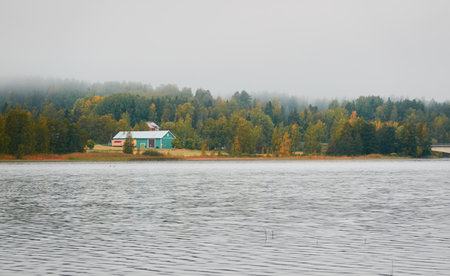 Lonely wooden farm house or shed in a fog at sunrise. Forest lake, meadow, overgrown agricultural field. Atmospheric autumn landscape. Finland. Nature, ecotourism, remote places themesの写真素材