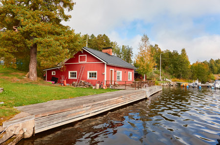 Wooden house colored with falu red dye. Motor boats, cutters and small fishing boats moored to a pier in a camping site. Forest in the background. Suiro lake (Kulovesi), Finland. Nature, ecotourismの写真素材