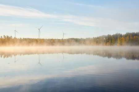 Forest lake in a morning fog. Wind farm, wind turbine generators. Clear blue sky, sunshine. Finland. Scandinavia, Europe. Autumn landscape. Nature, ecology, alternative and renewable energyの写真素材