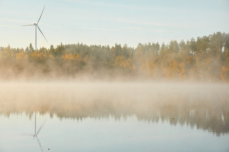 Forest lake in a morning fog. Wind farm, wind turbine generators. Clear blue sky, sunshine. Finland. Scandinavia, Europe. Autumn landscape. Nature, ecology, alternative and renewable energyの写真素材