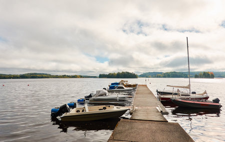Motor boats, cutters and small fishing rowing boats moored to a pier in a camping site. Forest in the background. Finland. Nature, vacations, recreation, ecotourism, lifestyle conceptsの写真素材