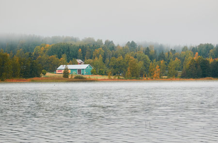 Lonely wooden farm house or shed in a fog at sunrise. Forest lake, meadow, overgrown agricultural field. Atmospheric autumn landscape. Finland. Nature, ecotourism, remote places themesの写真素材