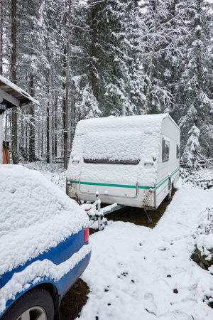 Caravan trailer parked in a snow-covered evergreen pine forest. First snow in autumn, early winter. Finland. Camping, ecotourism, vacations, weekend getaway, road trip themesの写真素材