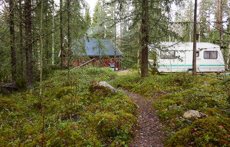 Caravan trailer (RV) parked near the wooden house. Evergreen pine forest. Autumn landscape. Finland. Camping, ecotourism, vacations, weekend getaway, road trip themesの写真素材