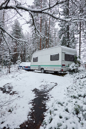 Caravan trailer parked in a snow-covered evergreen pine forest. First snow in autumn, early winter. Finland. Camping, ecotourism, vacations, weekend getaway, road trip themesの写真素材