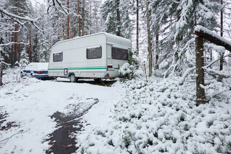 Caravan trailer parked in a snow-covered evergreen pine forest. First snow in autumn, early winter. Finland. Camping, ecotourism, vacations, weekend getaway, road trip themesの写真素材