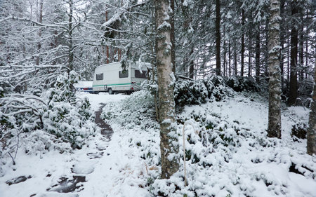 Caravan trailer parked in a snow-covered evergreen pine forest. First snow in autumn, early winter. Finland. Camping, ecotourism, vacations, weekend getaway, road trip themesの写真素材