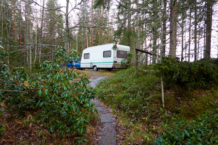Caravan trailer (RV) and a car parked in the evergreen pine forest. Autumn landscape. Finland. Camping, ecotourism, vacations, weekend getaway, road trip themesの写真素材