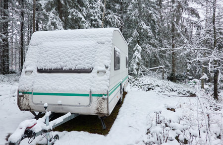 Caravan trailer parked in a snow-covered evergreen pine forest. First snow in autumn, early winter. Finland. Camping, ecotourism, vacations, weekend getaway, road trip themesの写真素材