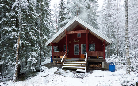 Traditional wooden house colored with falu red dye. First snow in autumn. Early winter. Evergreen forest, mighty pine and spruce trees. Finland. Nature, ecology, eco tourismの写真素材