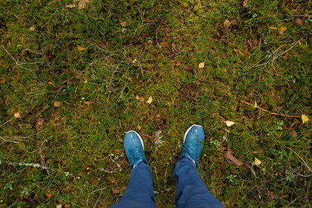 Man standing on the ground. Blue jeans and trekking boots. Green grass, golden leaves. Forest park. Concept landscape. Lifestyle, outdoors, leisure activities, sport, ecotourismの写真素材