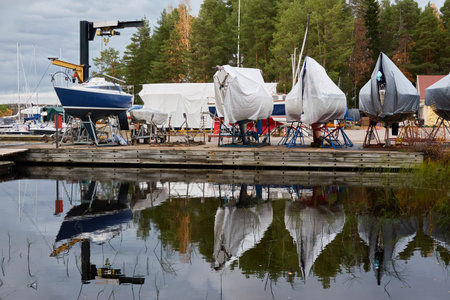 Sailboats moored to a pier and standing on land in a yacht marina prepared for winterization or new sailing season. Transportation, repair and service conceptsの写真素材