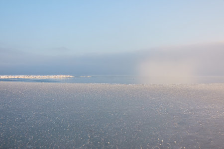 A view from the frozen snow-covered Baltic sea shore. Cloudy day, dramatic light, soft sunlight. Ice, snow. Fickle weather, blizzard. Winter tourism, global warming, climate change, ecology themesの写真素材