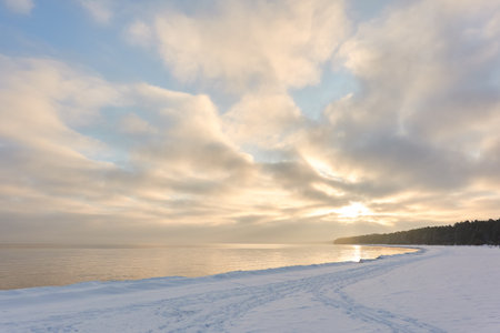 A view from the frozen snow-covered Baltic sea shore. Cloudy day, dramatic light, soft sunlight. Ice, snow. Fickle weather, blizzard. Winter tourism, global warming, climate change, ecology themesの写真素材
