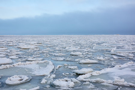 A view from the frozen snow-covered Baltic sea shore. cloudy day. Crystal clear water, cracked ice. Fickle weather, snowstorm, blizzard. Winter tourism, global warming, climate change, ecology themesの写真素材