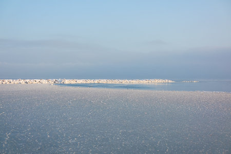A view from the frozen snow-covered Baltic sea shore. Cloudy day, dramatic light, soft sunlight. Ice, snow. Fickle weather, blizzard. Winter tourism, global warming, climate change, ecology themesの写真素材