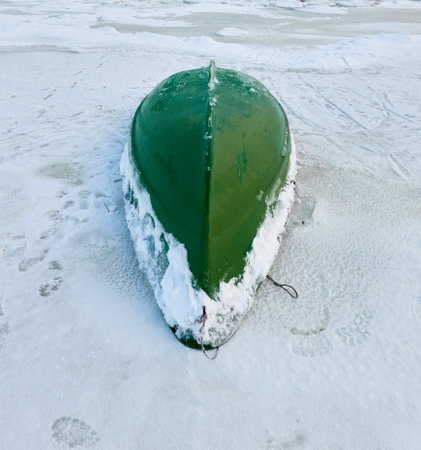 Green rowing fishing boat standing on land. Frozen Baltic seashore. Snow, ice, cloudy day. Concept winter landscape. Nature, environment, ecology, pollution themesの写真素材