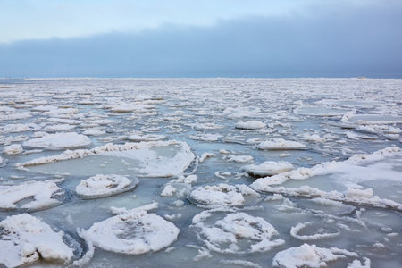 A view from the frozen snow-covered Baltic sea shore. cloudy day. Crystal clear water, cracked ice. Fickle weather, snowstorm, blizzard. Winter tourism, global warming, climate change, ecology themesの写真素材