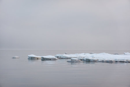 A view from the frozen snow-covered Baltic sea shore. cloudy day. Crystal clear water, cracked ice. Fickle weather, snowstorm, blizzard. Winter tourism, global warming, climate change, ecology themesの写真素材