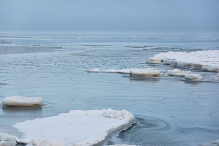 A view from the frozen snow-covered Baltic sea shore. cloudy day. Crystal clear water, cracked ice. Fickle weather, snowstorm, blizzard. Winter tourism, global warming, climate change, ecology themesの写真素材