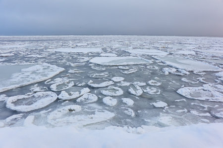 A view from the frozen snow-covered Baltic sea shore. cloudy day. Crystal clear water, cracked ice. Fickle weather, snowstorm, blizzard. Winter tourism, global warming, climate change, ecology themesの写真素材