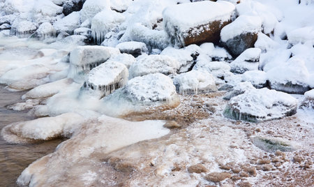 Frozen sea water surface texture, stones, icicles. Cloudy day, Ice, snow. Fickle weather, blizzard. Winter, global warming, climate change, ecology themesの写真素材