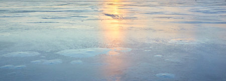 Cracked ice, snowflakes, snow, water surface, frozen lake shore. Sunset or sunrise. texture, close-up. winter scenery. Concept image, graphic resources. Nature, ecology, climate, global warmingの写真素材
