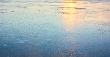 Cracked ice, snowflakes, snow, water surface, frozen lake shore. Sunset or sunrise. texture, close-up. winter scenery. Concept image, graphic resources. Nature, ecology, climate, global warmingの写真素材