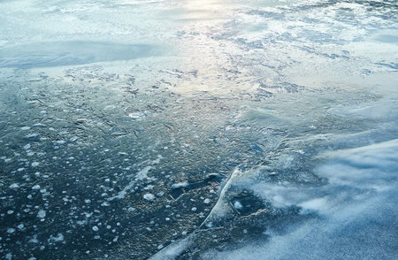 Cracked ice, snowflakes, snow, water surface, frozen lake shore. Sunset or sunrise. texture, close-up. winter scenery. Concept image, graphic resources. Nature, ecology, climate, global warmingの写真素材