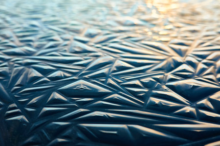 Cracked ice, dark water surface, frozen lake shore. Geometric natural pattern. Winter landscape, picturesque scenery. Concept image, graphic resources. Nature, ecology, climate, global warmingの写真素材