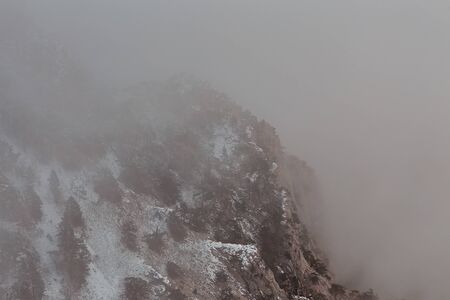 view from the cliff to the mountains with pine trees in the cloudsの写真素材