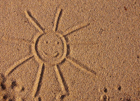 Smiling sun painted on the yellow sands of the sea on the beachの写真素材